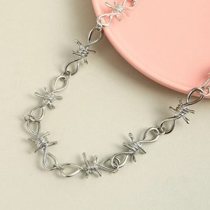 Silver thorn wire punk chain necklace with twisted barb design on pink ceramic plate