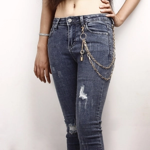 Detail of layered gold metal waist chain with ring and lock pendant on denim pants