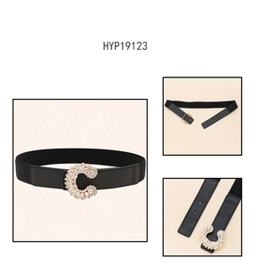 Detail of black elastic waist belt featuring a gold C-buckle with inlaid rhinestones