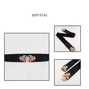 Detail of a black elastic waist belt with a golden flower buckle and white faux pearls