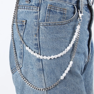 Détail d'une double chaîne en métal et perles d'imitation sur un jean en denim
