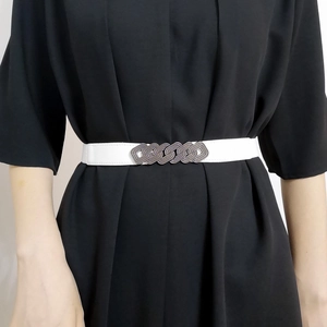 Detail of white elastic waist belt for women with interlocking oval metal buckle design
