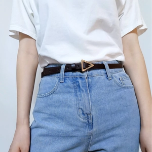 Detail view of dark brown slim leather belt with a golden triangle buckle on denim jeans