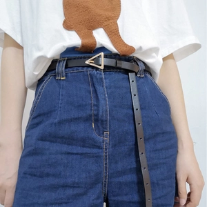 Detail of minimalist black leather belt with golden triangle buckle on denim jeans