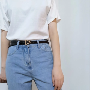 Close-up of minimalist black leather belt with a golden triangle buckle on jeans