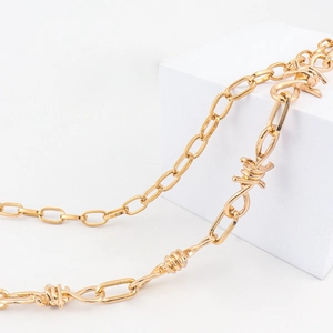 Detail van gouden dubbellaagse metalen hiphopketting met industriële doornelementen