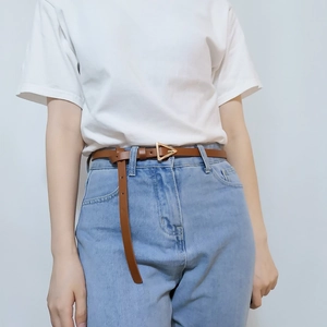Detail of slim brown leather belt with a golden triangle buckle on denim jeans