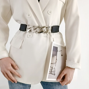 Dettaglio di cintura elastica nera con catena in metallo argento su un blazer bianco
