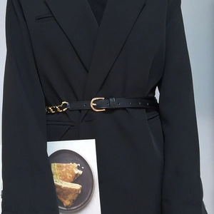 Detail eines schwarzen PU-Ledergürtels mit goldener Kette am Model mit schwarzem Blazer