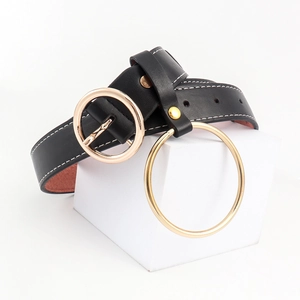 Détail d'une ceinture en cuir noir avec boucle ronde dorée, anneau décoratif et piqûres blanches