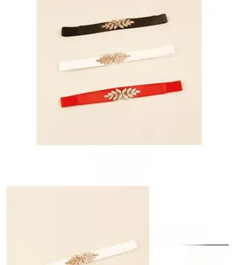Détail de la boucle feuille dorée et des ceintures élastiques en noir, blanc et rouge