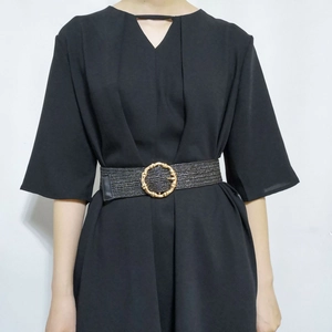 Detail of a black woven belt with a golden bamboo-texture round buckle on a black dress