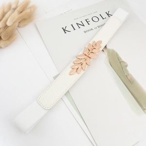 Détail d'une ceinture élastique blanche avec boucle feuille dorée sur fond de magazine