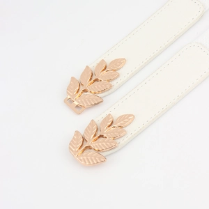 Détail de ceinture fine en cuir blanc avec boucle symétrique en forme de feuilles dorées