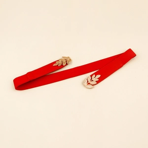 Détail de la boucle en métal doré en forme de feuille sur une ceinture élastique rouge