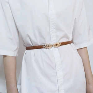 Detailed close-up of dark brown leather thin belt with elegant gold leaf-shaped buckle