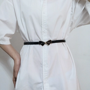 Detail of a thin black patent leather belt with a gold bow buckle on a white dress