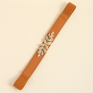 Détail d'une fine ceinture élastique avec boucle feuille dorée et empiècements en cuir