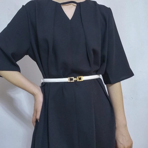 Detail view of a white slim leather belt with a gold metal buckle on a black dress