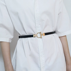 Detail of slim black leather waist belt with gold round buckle on white shirt