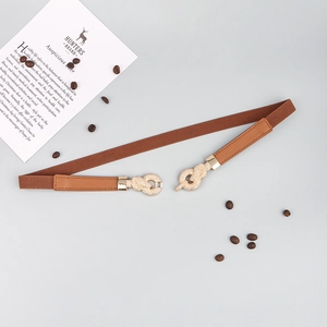 Detail of a thin elastic brown belt featuring a gold knotted buckle with sparkling crystals