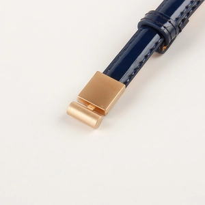 Macro detail of dark blue patent leather belt with matte gold geometric metal buckle