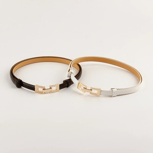 Detail of minimalist skinny waist belts in black and white with interlocking gold buckles