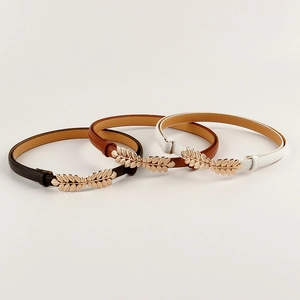 Detailed view of women's elastic waist belts in black, brown and white with leaf buckles