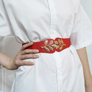 Close-up of red elastic belt featuring golden leaf buckle on a white shirt