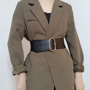 Close-up of wide black leather belt with large oval gold buckle on a brown blazer