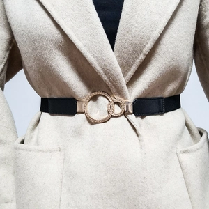 Detail of black elastic belt with golden double ring buckle on a beige coat