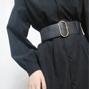 Detail of a wide black leather waist belt with an oval gold buckle on a black dress