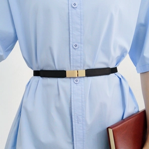 Close-up of a slim black elastic belt with a gold rectangular buckle on a light blue dress