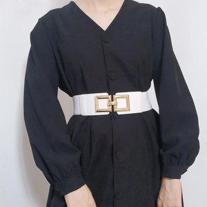 Close-up of a white elastic wide belt featuring a large gold square buckle on a black dress