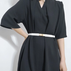 Detail of slim white elastic belt with gold square buckle on a black dress
