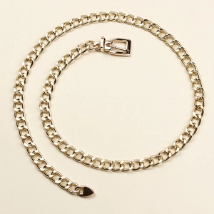 Flat gold metal link chain belt with square buckle and heart pendant on beige surface