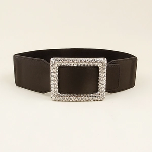 Detail of a wide elastic black belt featuring a large square buckle with sparkling rhinestones