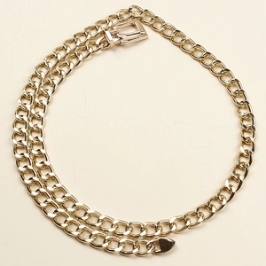 Detail of the golden metal chain belt featuring a classic buckle on a neutral background