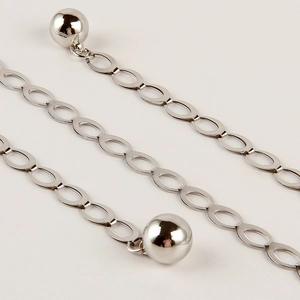 Détail d'une chaîne de taille en métal argenté avec maillons ovales et pendentifs boules