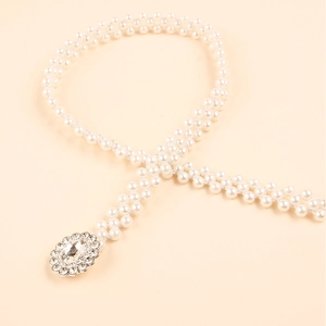 Detail of woven pearl belt featuring a sparkling oval rhinestone buckle on beige background