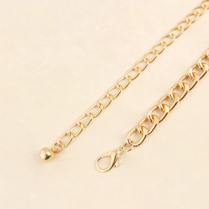 Detailed close-up of golden metal chain belt featuring lobster clasp and round charm