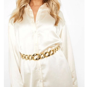 Close-up of golden chunky chain waist belt styled on a champagne satin shirt