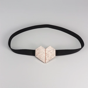 Détail de la boucle dorée en forme de cœur avec strass sur une ceinture élastique noire