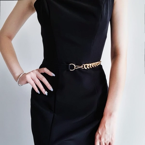 Detail of a high-elastic gold chain belt styled on a black slim-fit sleeveless dress