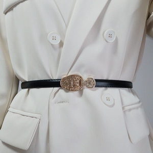 Détail de ceinture en cuir noir avec boucle dorée ajourée sur un costume blanc élégant