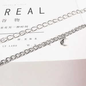 Detail of silver chain body jewelry with a polished crescent moon pendant on white book