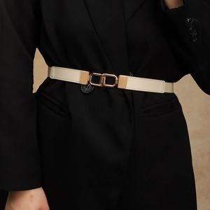 Close-up of cream elastic belt with gold interlocking buckle on black blazer