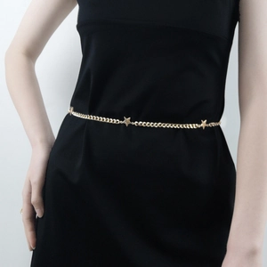 Detail of a thin gold metal waist chain with stars worn over a black dress for women