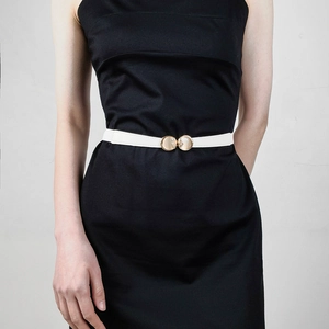 Detail eines dünnen weißen elastischen Gürtels mit goldener Opalschnalle am schwarzen Kleid