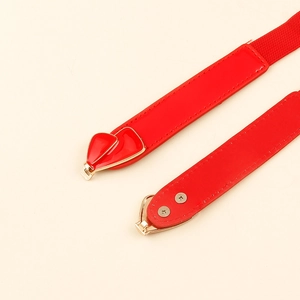 Detail of red elastic waist belt featuring a gold heart buckle and red enamel inlay